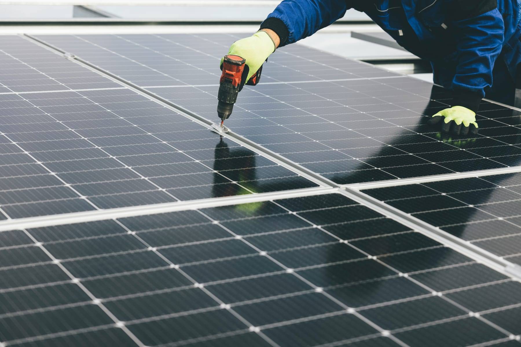 Installateur met werkhandschoenen zet zonnepanelen vast met een accuboormachine