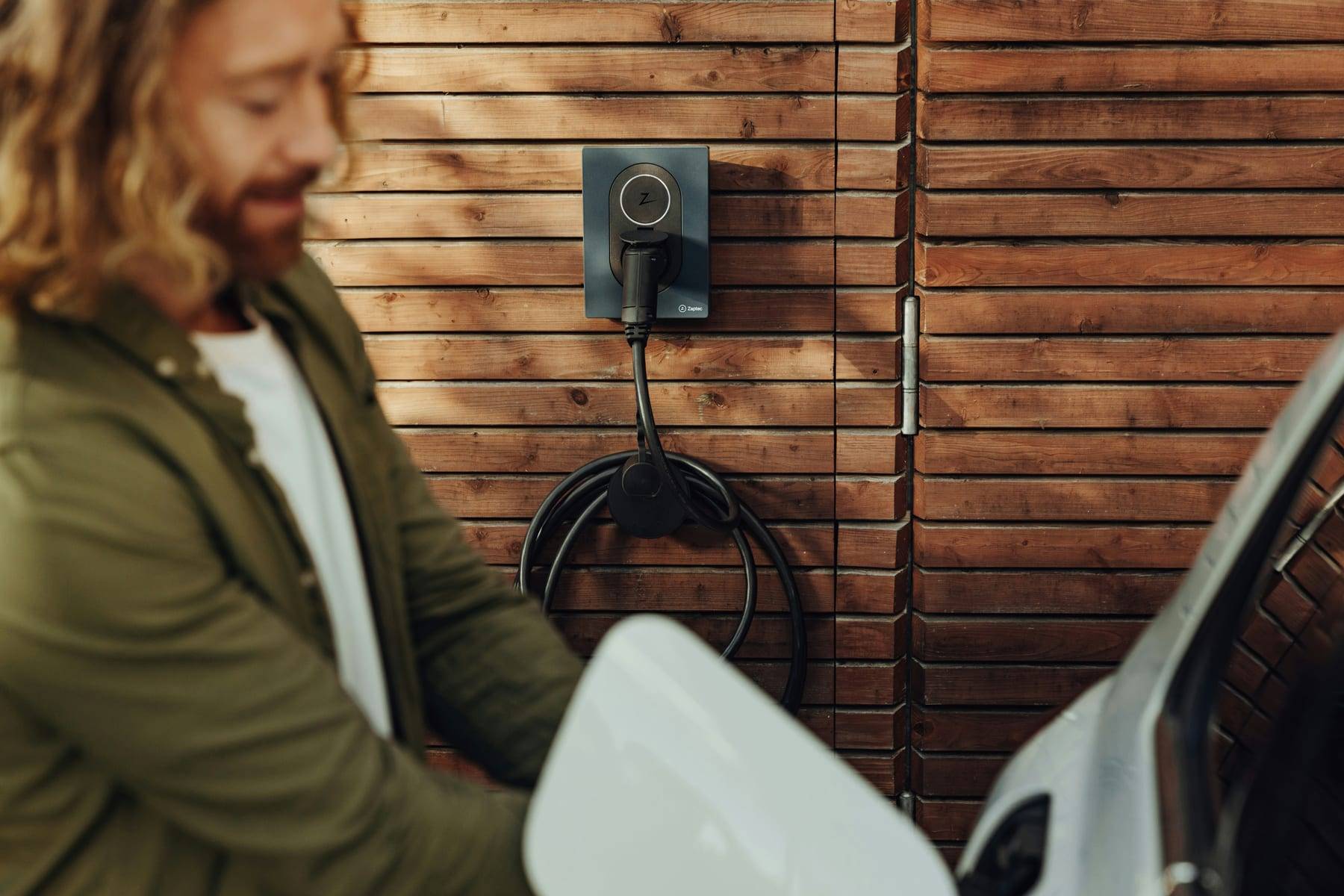 Man laadt zijn elektrische auto op bij een Zaptec-laadpaal aan een houten gevel