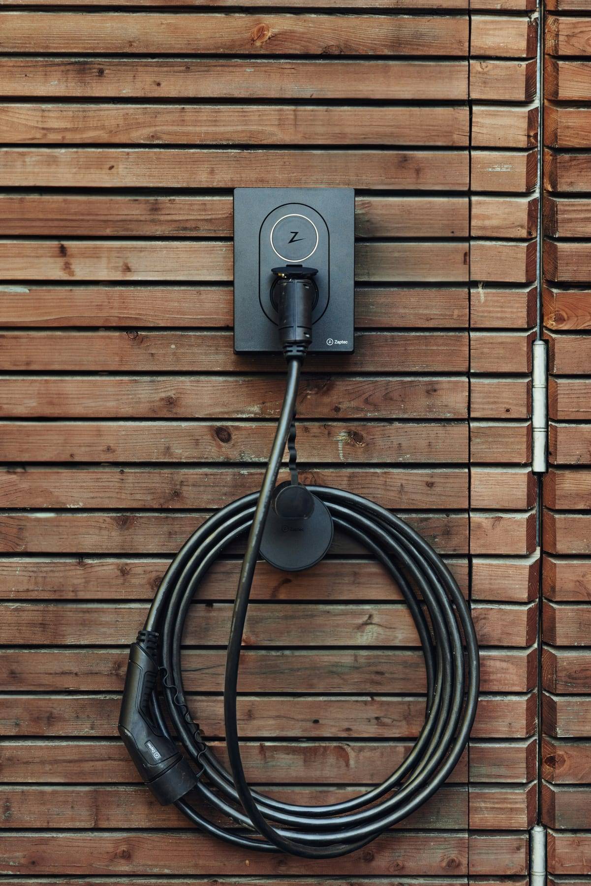 Zaptec-laadpaal op een houten gevel, met de laadkabel netjes opgerold